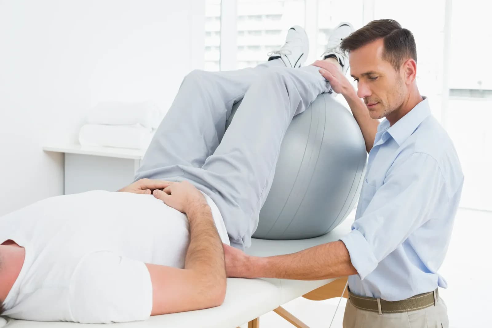 Physiotherapist helping a man exercise with his legs on an exercise ball