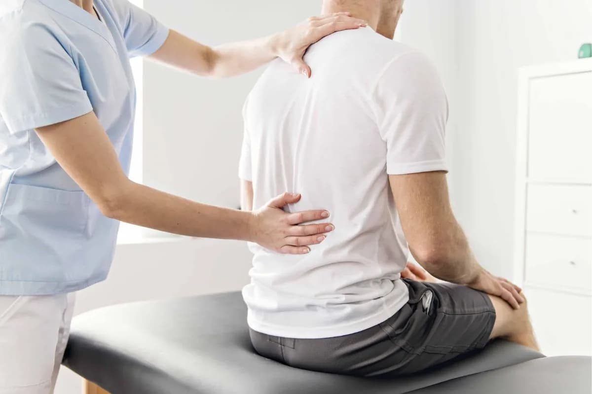 Physiotherapist examining a seated man's lower back